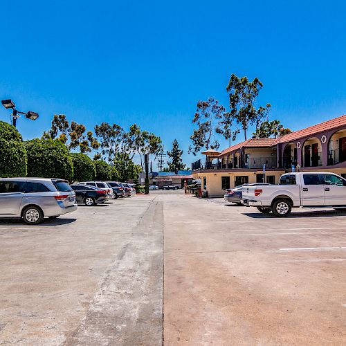 The image depicts a parking lot of a motel or hotel with several parked vehicles and rooms on the right side under a clear blue sky.