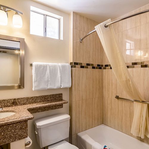 A modern bathroom with a granite countertop, towel rack, illuminated mirror, toilet, bathtub, shower curtain, and tiled walls ending the sentence.
