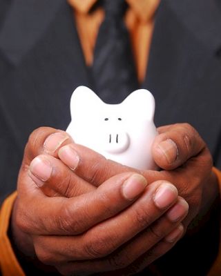 A person in a suit holding a white piggy bank with both hands.